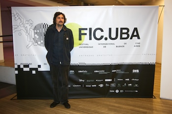 Un hombre de pie frente a un banner publicitario blanco y negro con el texto FIC.UBA y logotipos institucionales