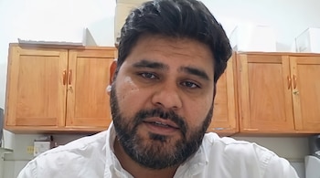 Un hombre con barba corta y camisa blanca frente a muebles de madera colgados en la pared.