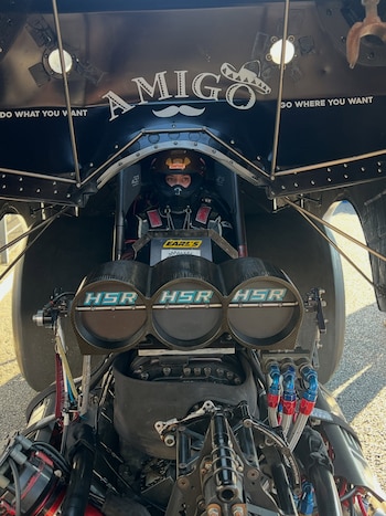 Piloto con casco dentro de un vehículo Funny Car con la carrocería abierta y el sistema de admisión del motor al frente
