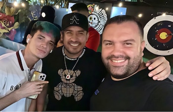 Tres hombres posan sonrientes para una selfie: uno a la izquierda con cabello bicolor, otro al centro con gorra negra y uno a la derecha con barba