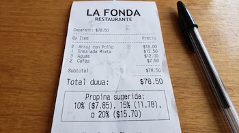 Recibo impreso con un recuadro de propina sugerida de 10%, 15% y 20% junto a un bolígrafo negro sobre madera.