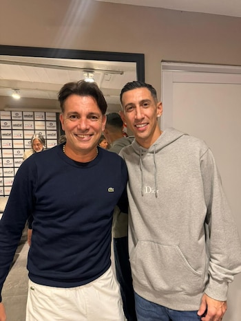 Martín Bossi con un suéter azul y Ángel Di María con una sudadera gris sonríen de pie uno al lado del otro