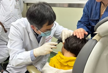El Dr. Yilai Shu examina a un paciente joven en el Hospital de Ojos y Otorrinolaringología de la Universidad de Fudan en China. (General de Massachusetts Brigham)