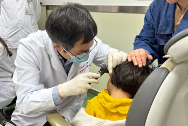 El Dr. Yilai Shu examina a un paciente joven en el Hospital de Ojos y Otorrinolaringología de la Universidad de Fudan en China. (General de Massachusetts Brigham)