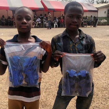 Dos niños de pie sostienen bolsas de plástico transparentes que contienen sandalias de color azul