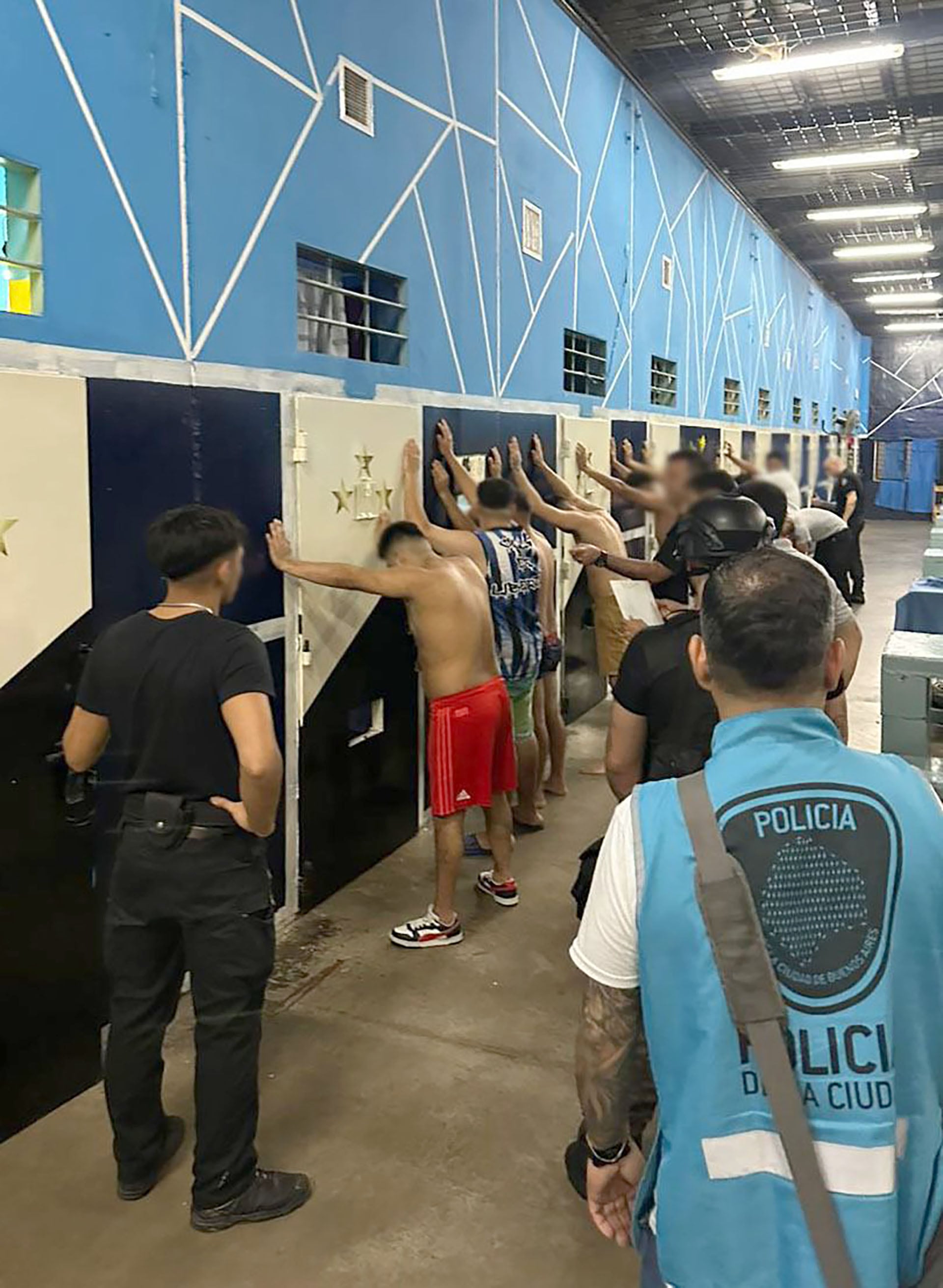 Agentes de la Policía de la Ciudad inspeccionan a hombres contra una pared durante un operativo para desarticular una red de extorsión sexual que operaba desde los penales de Sierra Chica y Merlo.