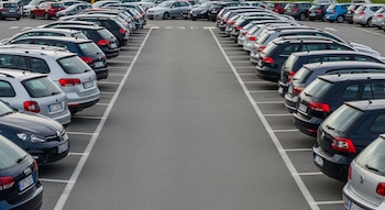 Vista aérea de dos largas filas de autos estacionados de culata en un amplio aparcamiento al aire libre con pavimento gris y líneas blancas.
