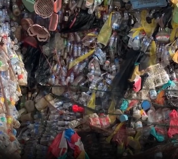 Pared compacta formada por numerosas botellas de plástico transparentes, bolsas de colores, cestas y redes de sujeción