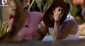 Primer plano de Diego Chávarri llorando y cubriéndose el rostro con un sombrero de vaquero; otro hombre con camiseta rosa y gafas lo observa