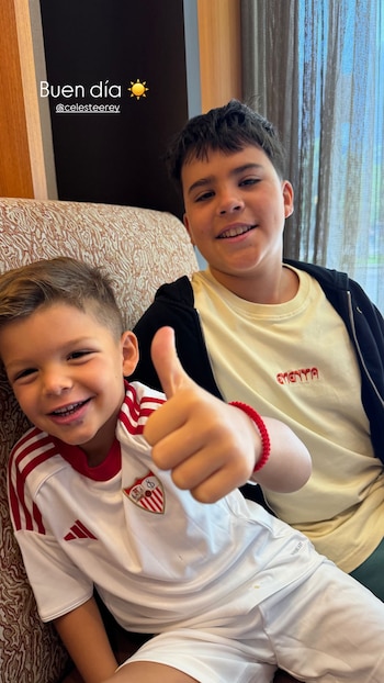 Dos niños posan sonriendo. El niño de la izquierda viste camiseta blanca y roja con escudo y levanta el pulgar. El niño de la derecha lleva camiseta beige y sudadera negra