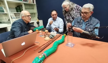 Cuatro personas, tres hombres y una mujer, sentadas alrededor de una mesa con un portátil, micrófonos y diversos objetos culturales y artesanías