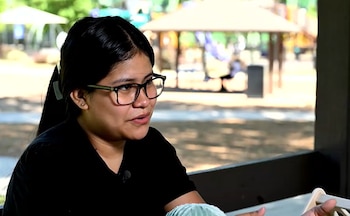 Primer plano de Edith, una mujer con cabello oscuro recogido y gafas de montura negra, vestida con camiseta negra, hablando. Fondo borroso de parque