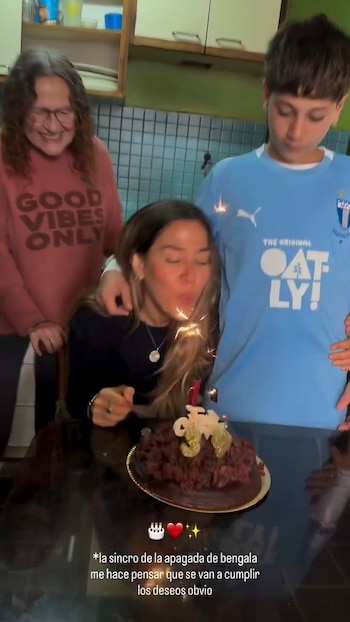 Jimena Barón sopla una bengala encendida en un pastel de chocolate oscuro con el número 36, mientras una mujer y un joven sonríen a su lado en una cocina