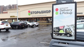 Vista externa de uma loja Stop & Shop com placas de entrega e retirada, e diversos veículos, como SUVs e tanques, em estacionamento molhado.