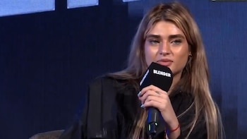 Primer plano de Marta Fort, joven de cabello rubio, sosteniendo un micrófono negro con el logo 'BLENDER' y hablando