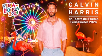 Un hombre con camisa rosa y pantalón celeste posa. Detrás, una rueda de la fortuna iluminada, flamencos y luces de feria, con un filtro naranja.