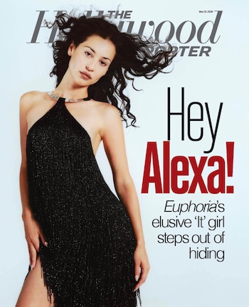 Una mujer joven con cabello oscuro y ondulado, vestida con un vestido halter negro brillante con flecos y un collar plateado, posa en una portada de revista