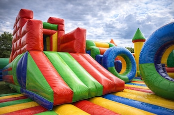 Juego inflable grande con toboganes y formas en rojo, verde, azul y amarillo, sobre césped verde, bajo un cielo con nubes.