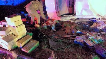 Pintura acrílica de una escena nocturna con una figura agachada cerca de un vehículo volcado, rodeada de cajas y escombros. Luces de emergencia iluminan el cuadro