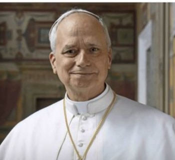 Primer plano del Papa León XIV, un hombre con sotana papal blanca y cadena de oro, sonriendo ligeramente. El fondo muestra una pared decorada