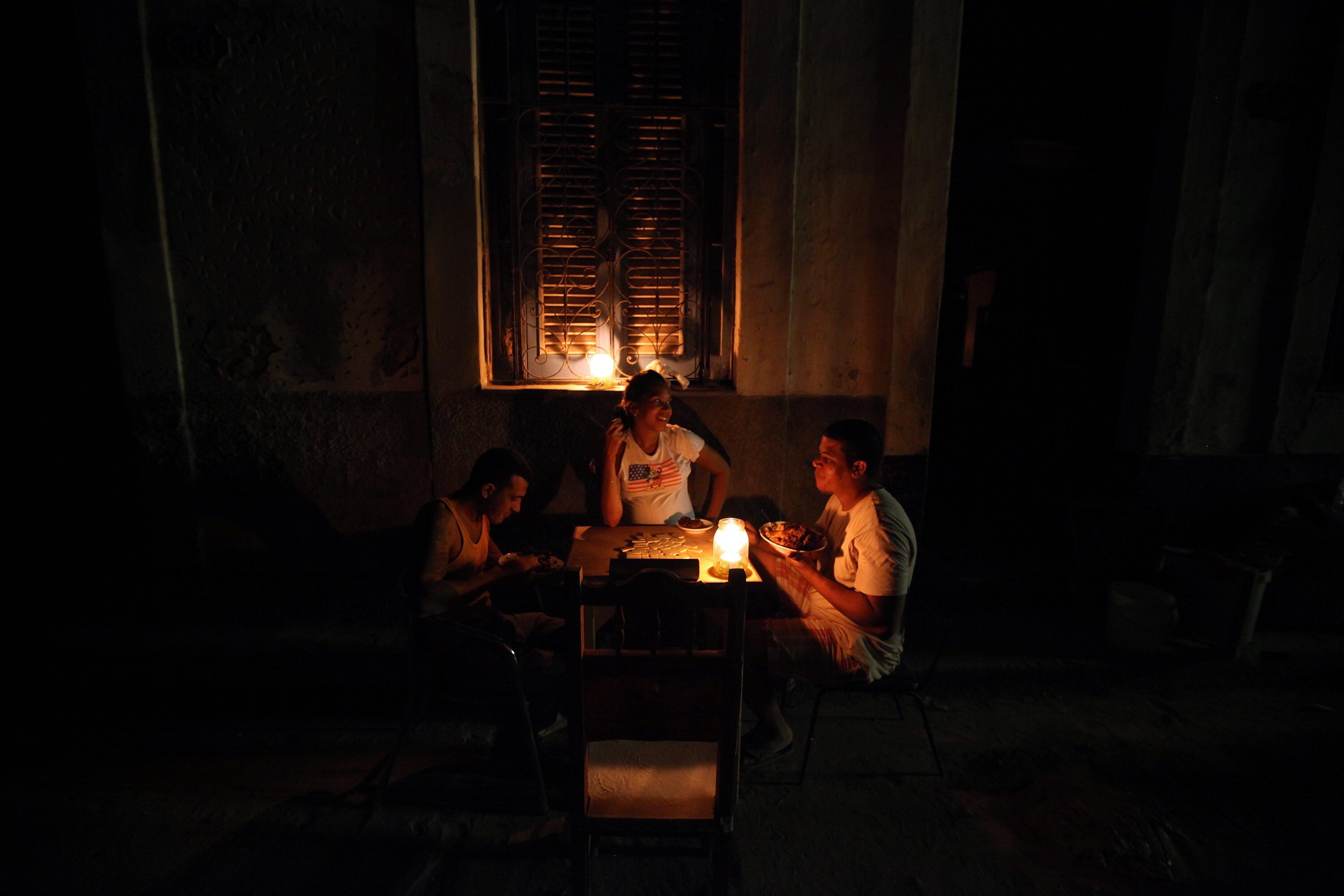 Tres personas comen en una calle sin iluminación eléctrica, durante uno de los diarios apagones, en La Habana (EFE/Alejandro Ernesto)