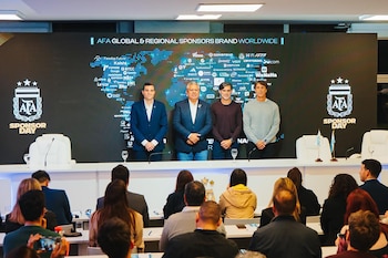 Cuatro hombres en un podio frente a una pantalla con logos de marcas, un mapa mundial y emblemas de AFA. Una audiencia sentada asiste al evento