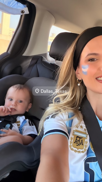 Mujer y bebé en asiento de coche. Ambos usan camisetas de fútbol de Argentina. Mujer con pintura facial. Un marcador indica 'Dallas, Texas'