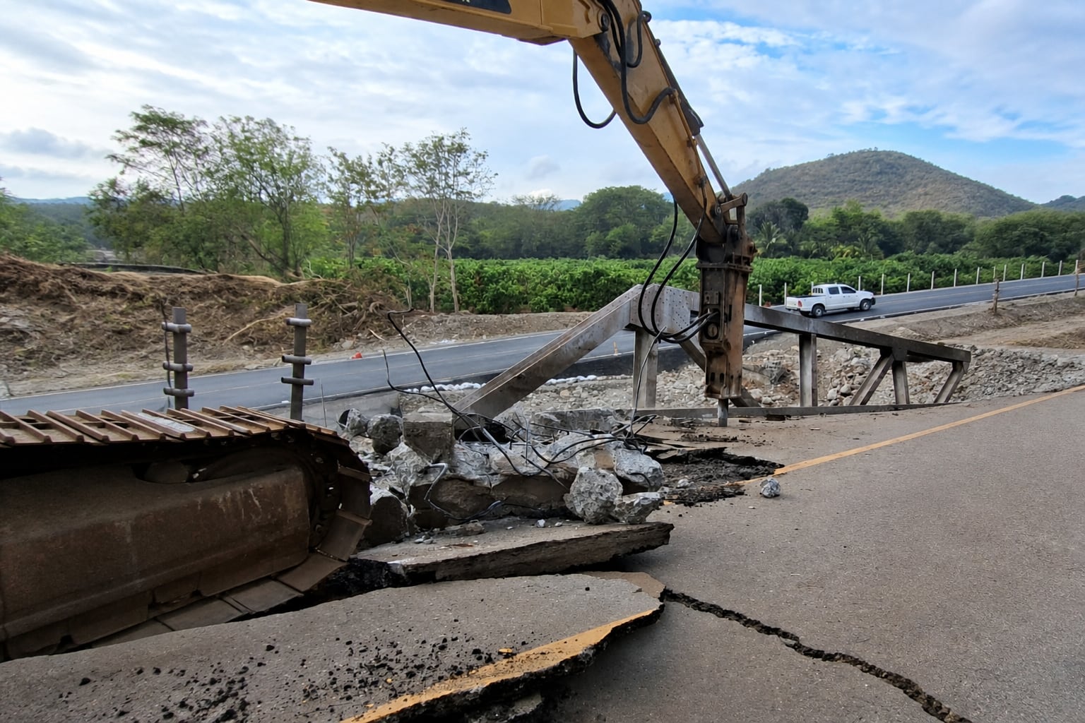 Una excavadora equipada con martillo hidráulico demuele la estructura de hormigón de un puente dañado junto a una carretera. (Imagen Ilustrativa Infobae)