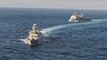 Dos buques de guerra grises navegan en el mar abierto. El buque trasero lleva una bandera peruana. Ambos dejan una estela blanca