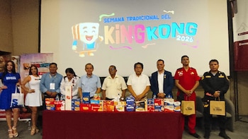Grupo de personas de pie frente a una mesa con cajas de dulce King Kong. Al fondo, una pantalla proyecta un logo de la Semana Tradicional del King Kong 2026