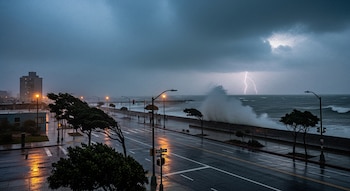 Vista de una ciudad costera bajo una tormenta. Lluvia intensa, calles mojadas, árboles inclinados por el viento, oleaje fuerte y un relámpago ilumina el cielo sobre el mar.