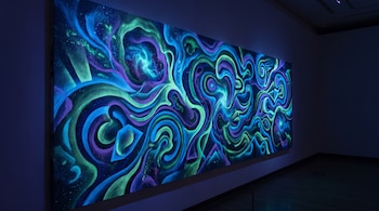 Mural abstracto dividido en paneles con patrones ondulados en colores azul, verde y violeta brillantes dentro de un recinto oscuro.