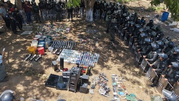Agentes policiales con equipo antidisturbios. En el suelo, diversos artículos confiscados: cubetas, botellas, altavoces, pantallas, celulares, cables y placas