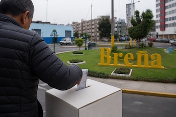 Un hombre deposita una cédula en una caja de votación frente a un letrero amarillo que dice Breña.