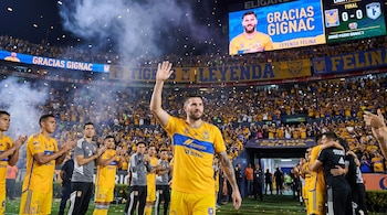 André-Pierre Gignac, con camiseta amarilla de Tigres, levanta la mano y saluda a la afición en un estadio lleno con confeti cayendo y pantallas con su imagen.