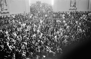 Fotografía en blanco y negro de una gran multitud de personas, principalmente jóvenes, llenando un auditorio con asientos escalonados y un suelo abarrotado