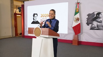Claudia Sheinbaum de pie tras un podio con el escudo mexicano, con una bandera nacional y una pantalla de fondo.