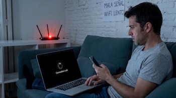 Hombre sentado en sofá con laptop mostrando 'Connection Lost'. Sostiene un teléfono. Router con luz roja visible y cartel 'MALA SEÑAL WIFI LENTO' en la pared.