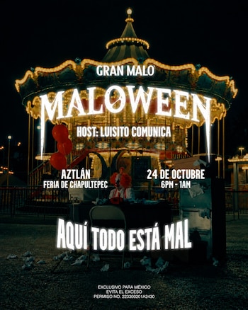 Un tiovivo iluminado de noche detrás de un payaso sentado frente a un escritorio con globos rojos y letreros superpuestos