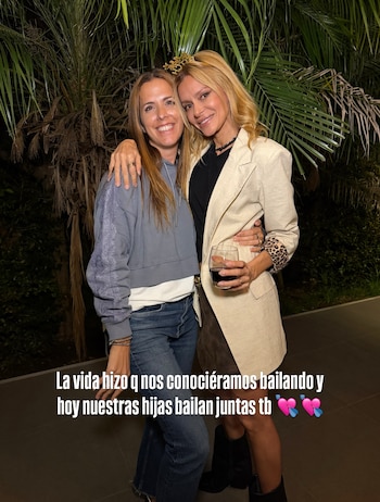 Dos mujeres abrazadas posan de noche frente a palmeras, una de ellas con una copa en la mano y una pequeña corona en la cabeza