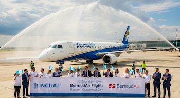 Grupo de personas frente a un avión BermudAir en una pista de aeropuerto, con arcos de agua y un banner de INGUAT celebrando el nuevo vuelo.