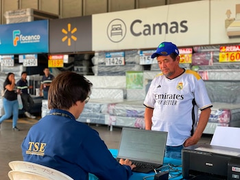 Un trabajador con chaqueta del Tribunal Supremo Electoral utiliza una computadora frente a un hombre dentro de una tienda