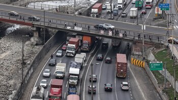 Vista superior de automóviles y camiones transitando en una carretera de varios carriles junto a un puente y letreros de señalización vial
