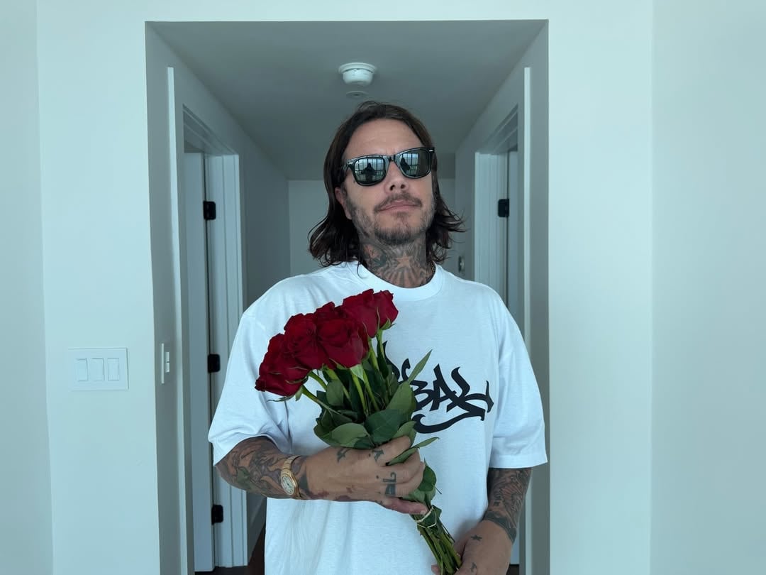 El productor Sebastián Ortega posa con un ramo de rosas rojas en un pasillo blanco, mostrando un gesto cariñoso.