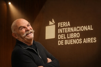 Un hombre sonriente con bigote aparece en primer plano junto a un panel con el texto Feria Internacional del Libro de Buenos Aires.