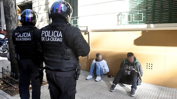 Vista trasera de dos policías de la Ciudad de Buenos Aires con cascos y chalecos oscuros, mirando a dos hombres sentados en el suelo con el rostro borroso