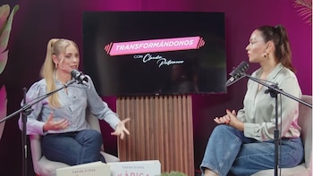 Dos mujeres están sentadas frente a frente, cada una con un micrófono. Detrás de ellas, una pantalla muestra el logo "Transformándonos con Claudia Portocarrero"