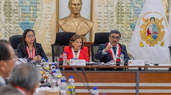 Tres autoridades sentadas ante una mesa con el escudo de la Universidad Nacional Mayor de San Marcos y un busto al fondo