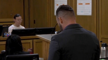 Vista parcial de una sala de tribunal con Trace Bradburn sentada frente a monitores, mientras un hombre de traje le da la espalda