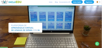 Computadora portátil sobre una mesa de madera que exhibe la página web de INCLUEDU junto a notas adhesivas, anteojos y una planta pequeña